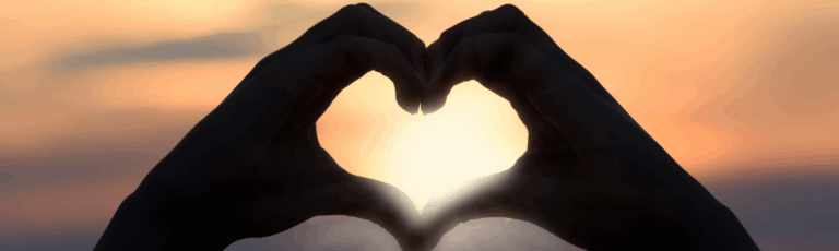 Silhouette of two hands forming a heart shape in front of a sunset, symbolizing the longing to meet anyone and the search for meaningful connection.