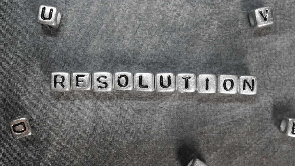 The word "Resolution" spelled out with metallic letter blocks on a gray background, emphasizing constructive conflict.