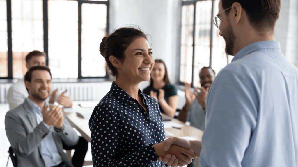 Smiling professional receiving a handshake and applause at work after a promotion