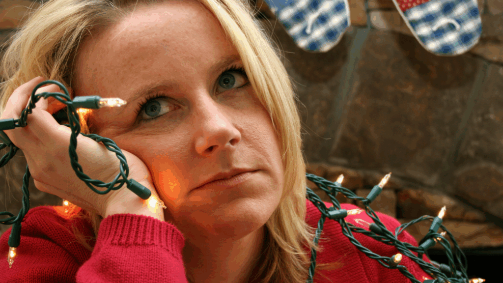 Woman holding holiday string lights, looking frustrated and stressed during the festive season.