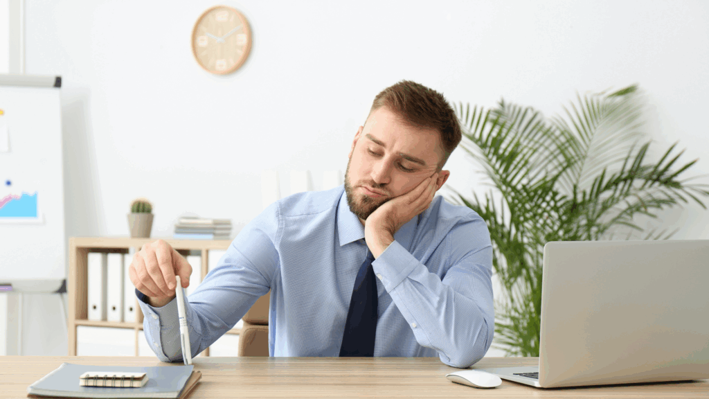 Man sitting at a desk appearing bored
Alt: Businessman sitting at a desk looking bored and unmotivated.