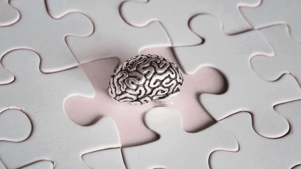 Metal brain model in white puzzle piece gap showing mind-body connection.