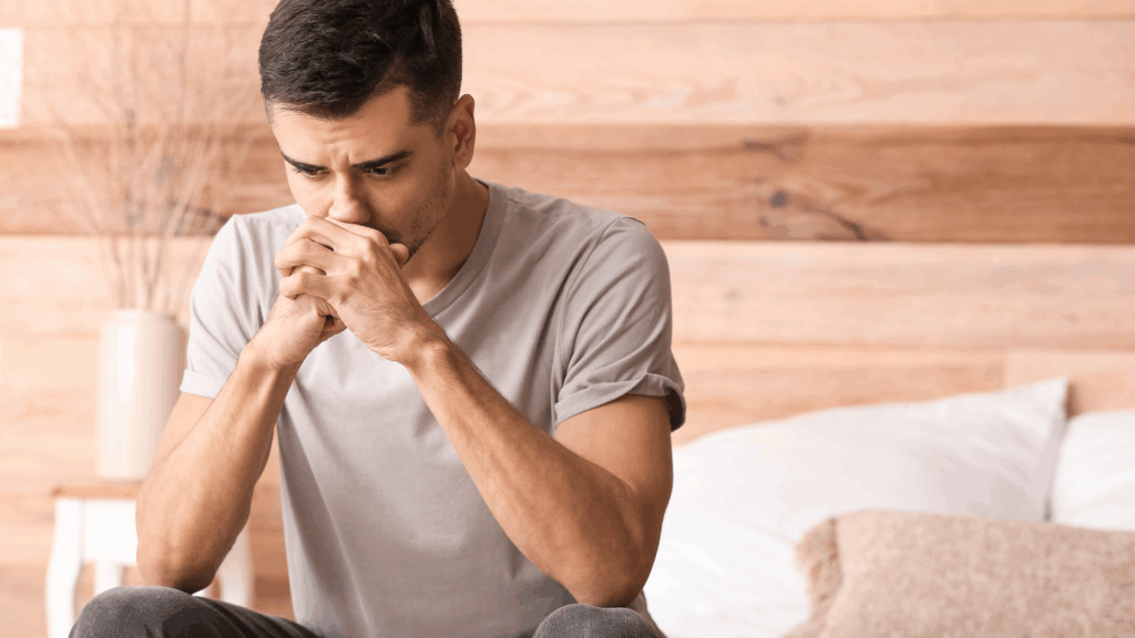 Man in white t-shirt deep in thought with hands clasped
