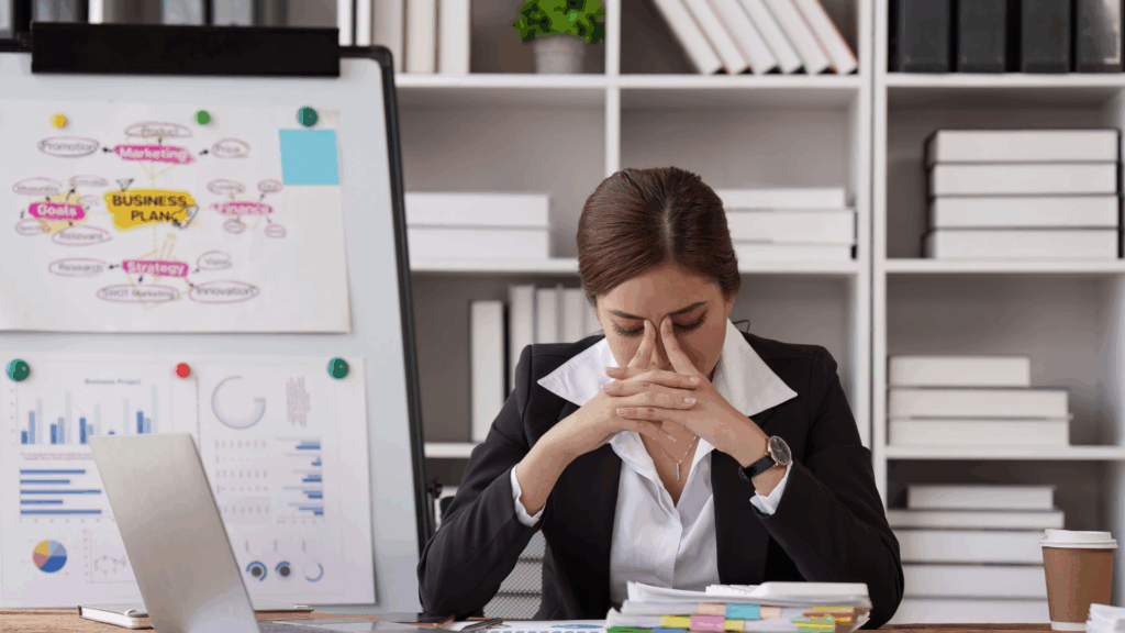 Professional woman experiencing stress at desk with business plan and charts
