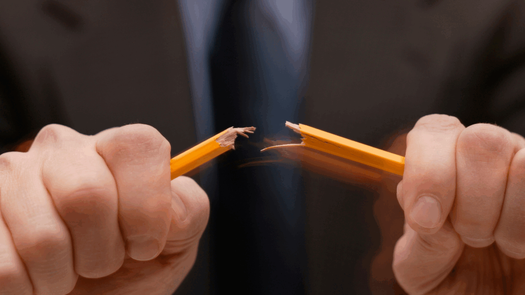 Close-up of a person snapping a pencil in frustration, symbolizing uncontrolled anger.