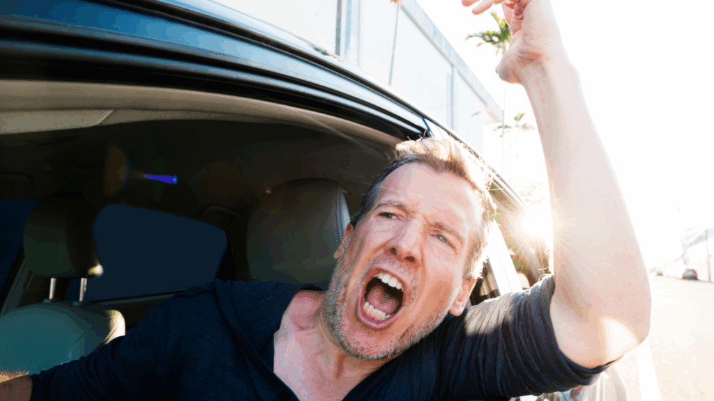 A frustrated man yelling out of a car window, illustrating road rage and reactive anger.