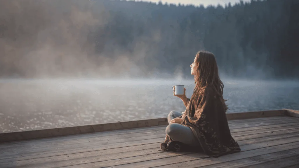 Person sitting peacefully by a lake with a cup, embodying the calm and clarity that follows a digital detox.