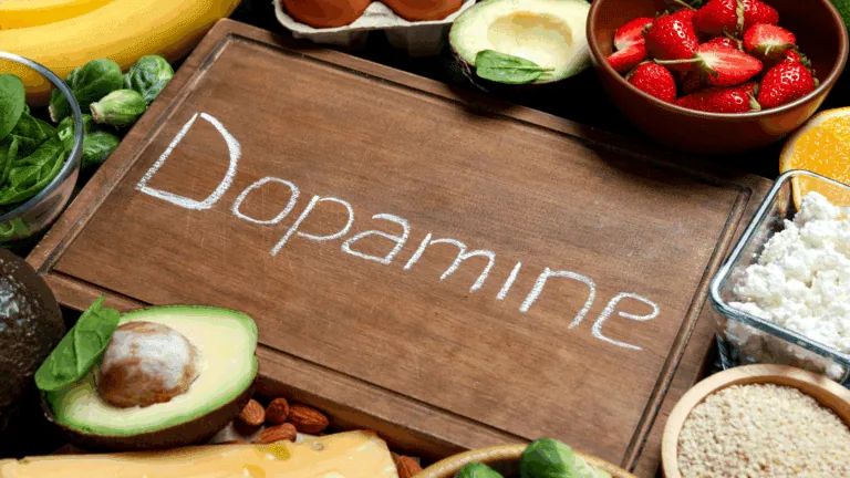 A selection of dopamine boosting foods including avocado, strawberries, eggs, spinach, and cheese arranged around a wooden board with Dopamine written on it.