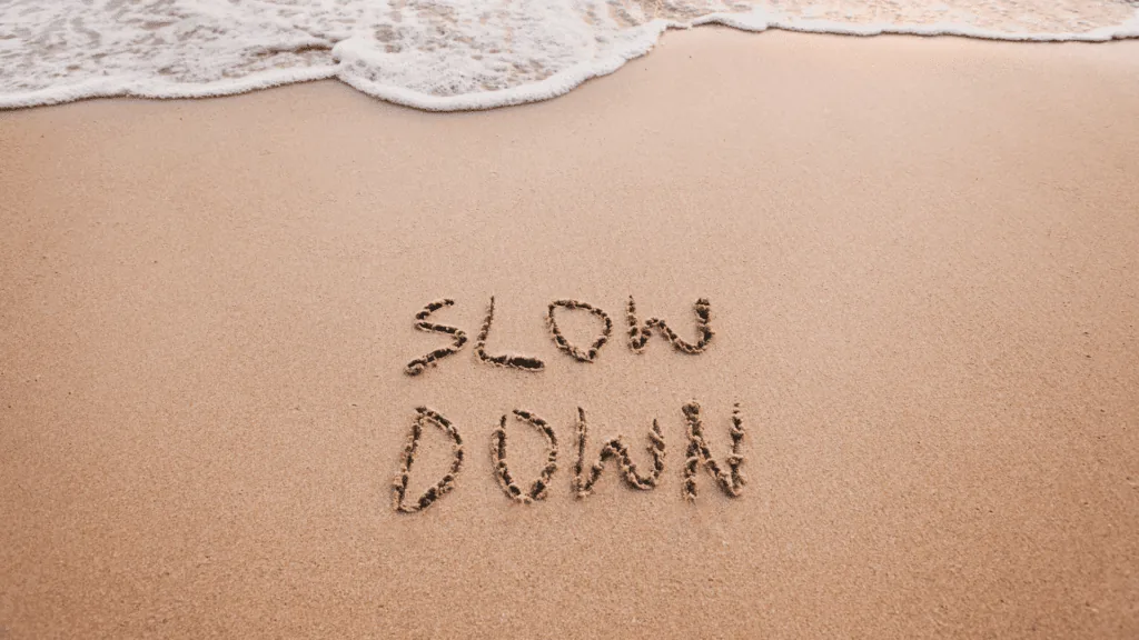 The words slow down written in the sand near gentle ocean waves.
