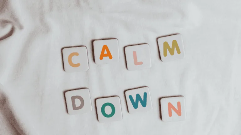 Tiles spelling out “calm down” on a white fabric background, symbolizing mindfulness of anxiety and emotional regulation.