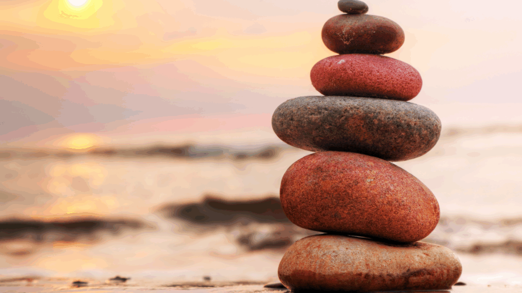 Stacked stones at sunset symbolizing balance, intentional awareness, and the choice to escape hustle culture.