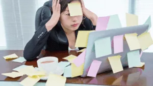 Stressed woman surrounded by sticky notes at her desk, highlighting challenges that impact leadership presence.