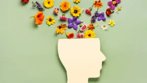 Colorful flowers emerging from a paper cutout head, symbolizing growth and well-being in youth mental health.