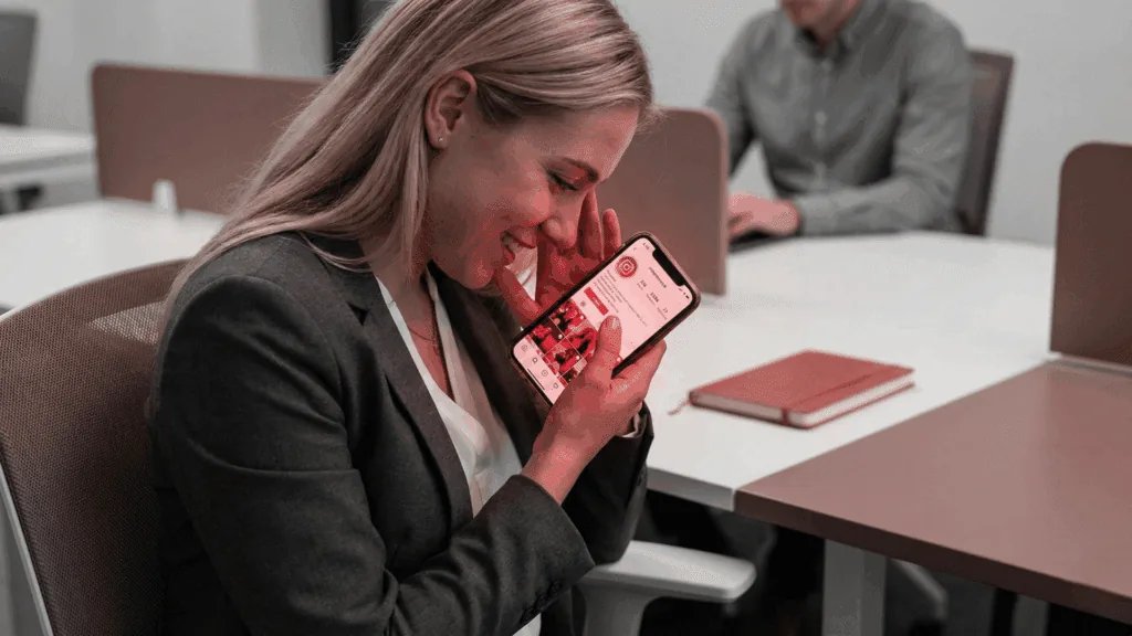 A smiling woman in an office looks at her phone with affection, capturing the emotional anticipation reflected in the neuroscience of love.