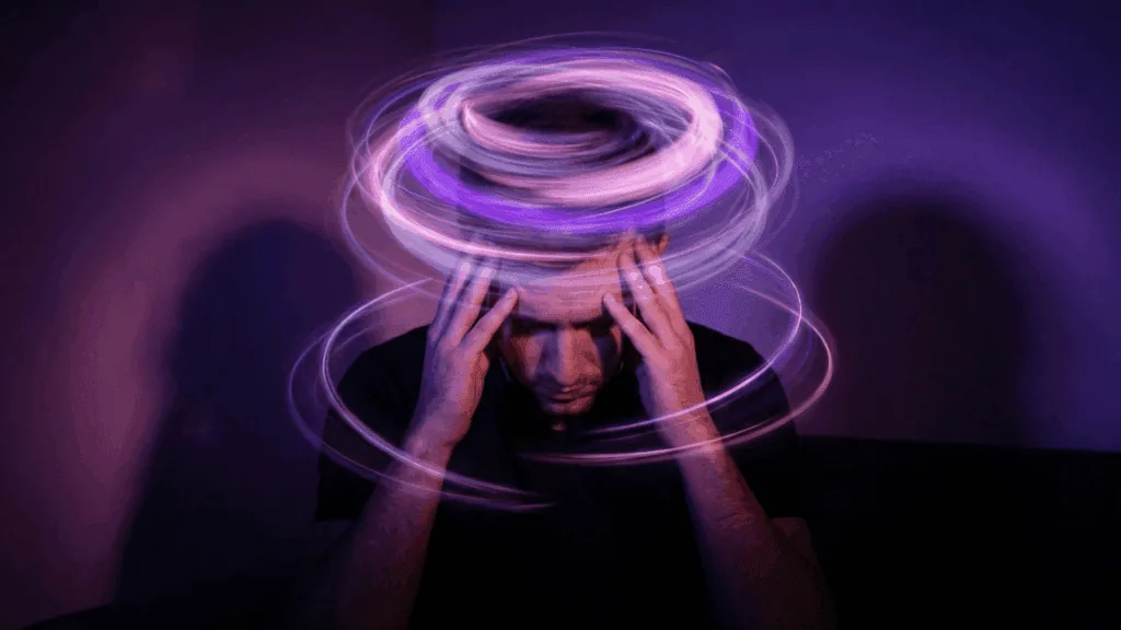 A man holds his head as glowing purple light trails spiral around his mind, representing the neuroscience of rumination.