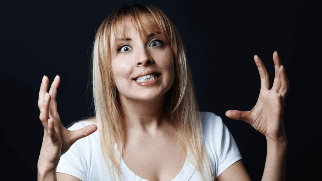 Angry woman with wide eyes and raised hands expressing surprise or shock.