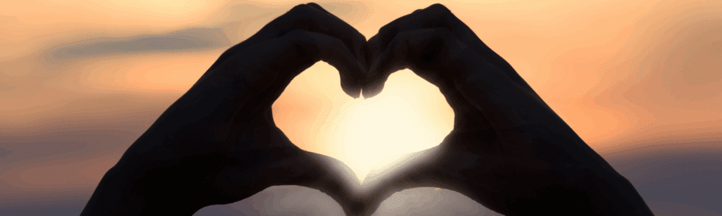 Silhouette of two hands forming a heart shape in front of a sunset, symbolizing the longing to meet anyone and the search for meaningful connection.