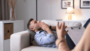 A man laying on a couch receiving brain-based coaching from a professional, experiencing Mental Exhaustion and Fatigue
