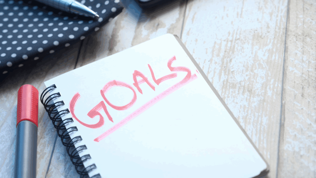 Close-up of a notepad with the word “Goals” written in red, representing the concept of a self-driving goal.