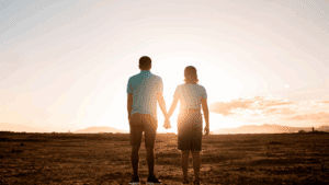 Couple holding hands while facing the sunset, symbolizing Embracing Vulnerability and connection.
