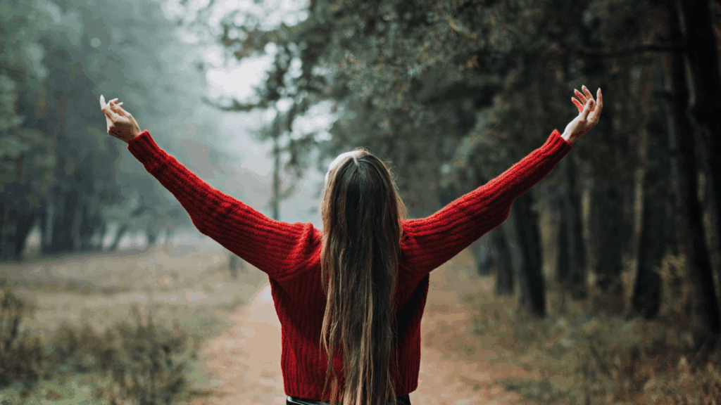 Woman in a red sweater with arms raised in nature, symbolizing freedom through neuroplasticity and cognitive restructuring.
