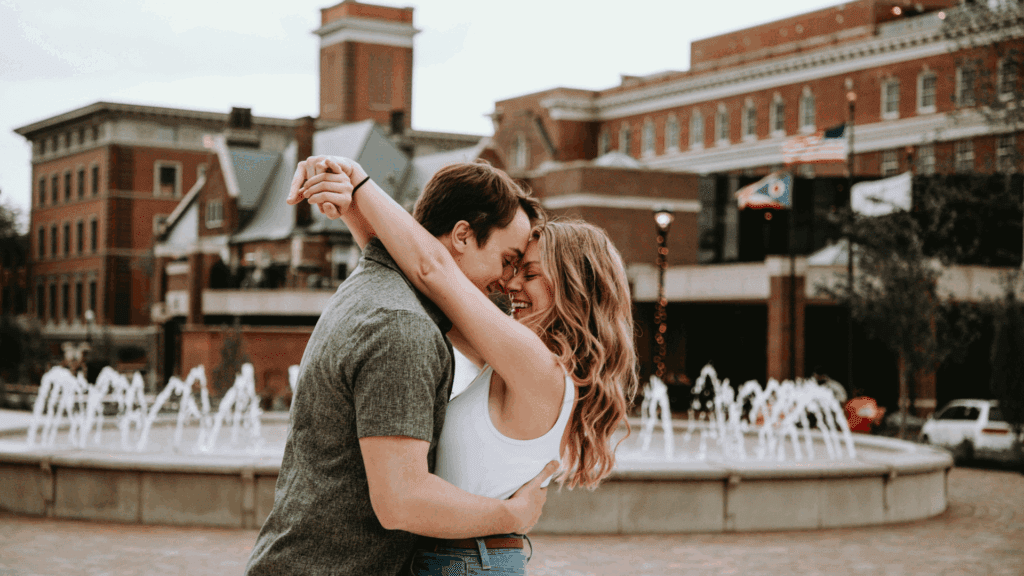 A smiling couple embracing near a fountain, symbolizing connection and the influence of neuroscience in love biases.