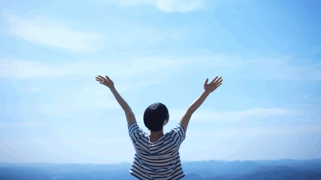 Person raising arms in triumph under a clear sky, symbolizing overcoming limiting beliefs.