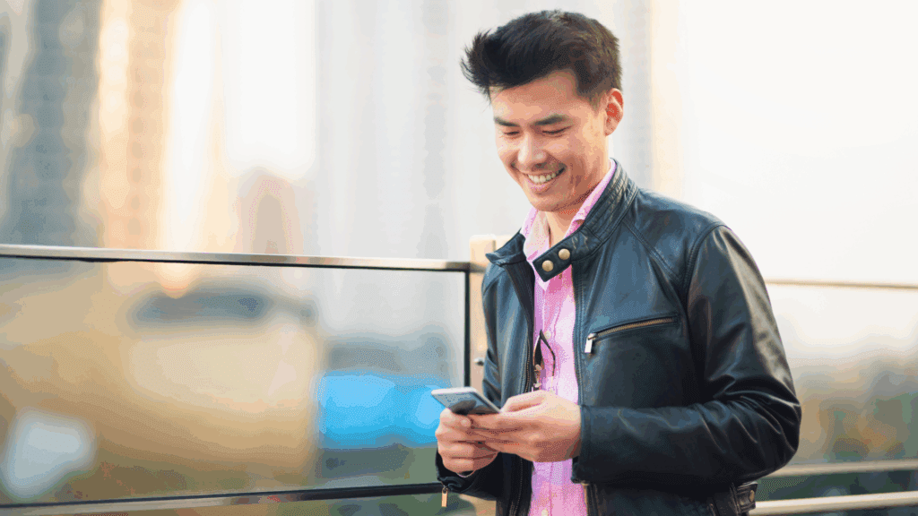 Smiling man in a leather jacket looking at his phone, representing ways to enhance your likability.