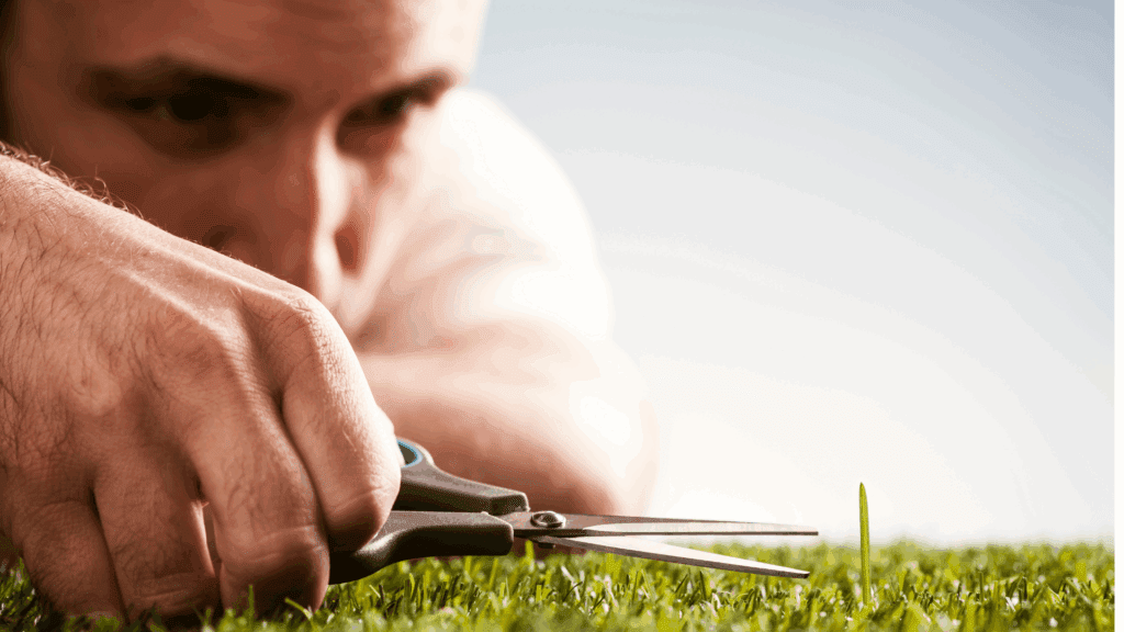A man cutting grass with scissors, showcasing the dark side of perfectionism