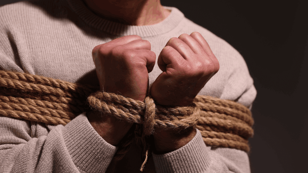 A man who has his hands tied up with rope indicating self-sabotage.