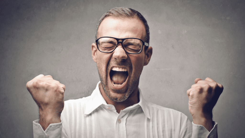 Man in white shirt and glasses expressing triumph after stoping self-defeating behaviors and succeeding.