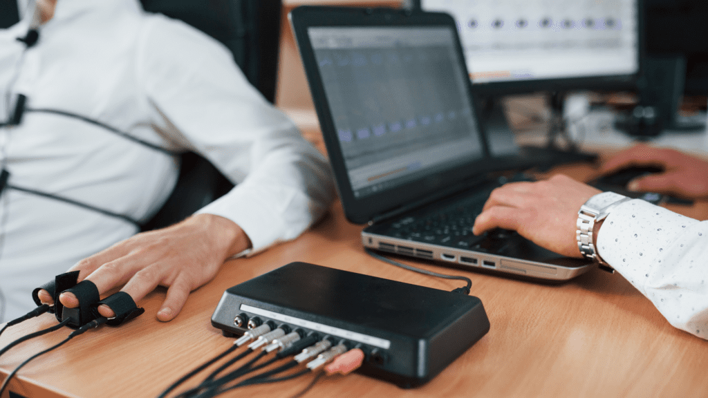 A person undergoing a polygraph test, with sensors attached to their hand and a computer analyzing the data.



