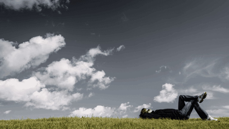 A person relaxing on the grass under a sky with both dark and light clouds, symbolizing the transition from rigid thought patterns to cognitive balance.