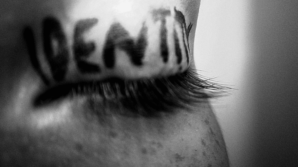 The word identity written across a closed eyelid in bold letters, symbolizing introspection and the struggle of a self-identity crisis.