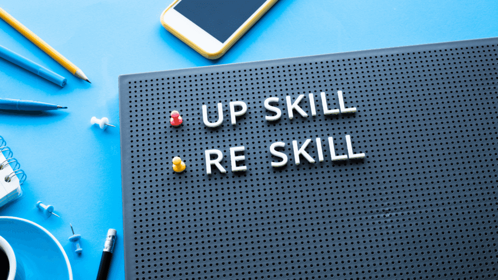 Reskilling concept board with office supplies and smartphone with the words up skill and re skill on it.