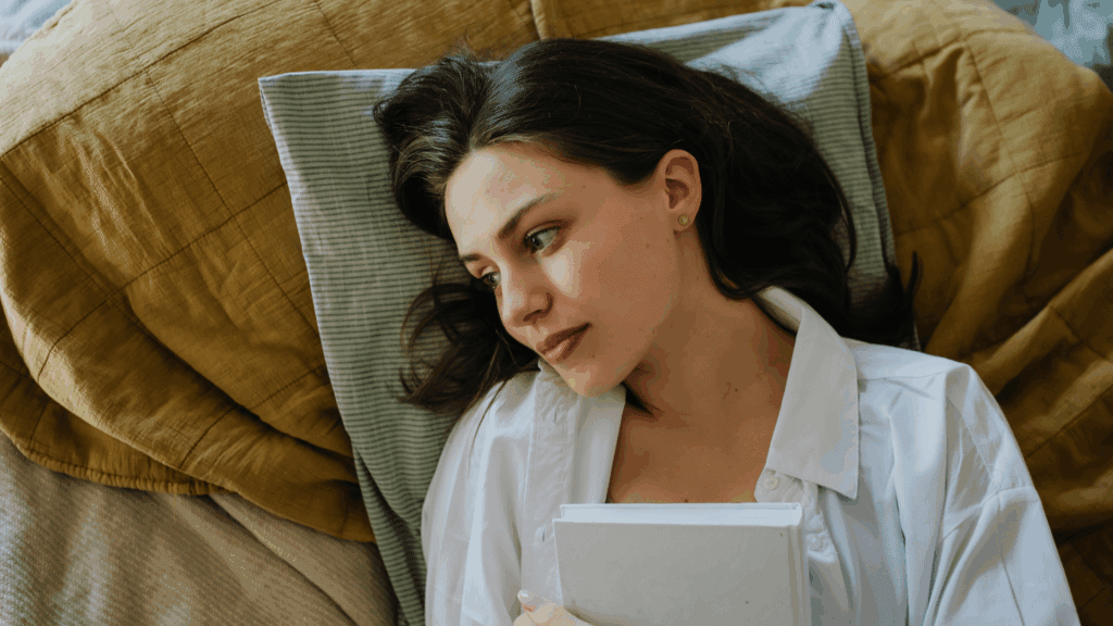 A woman holding book while reflecting on romantasy story.