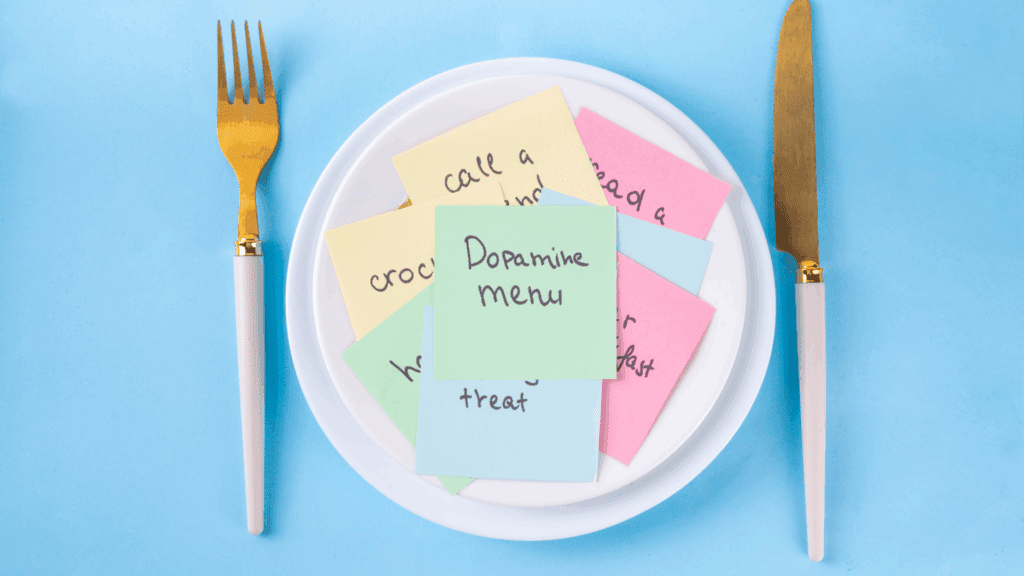 A plate with colorful notes labeled “Dopamine menu” surrounded by a gold fork and knife, symbolizing dopamine boosting foods choices.