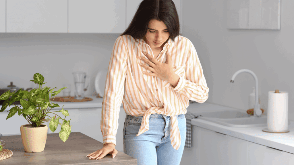 A woman standing in her kitchen, holding her chest and practicing mindful breathing to manage anxiety.
