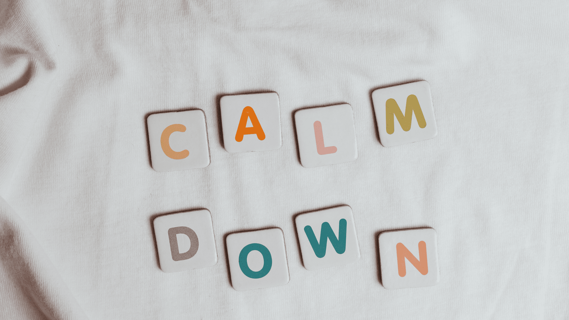 Tiles spelling out “calm down” on a white fabric background, symbolizing mindfulness of anxiety and emotional regulation.