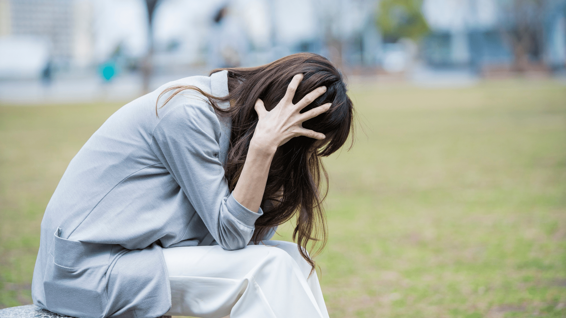 Woman sitting outdoors holding her head in distress, illustrating symptoms of anxious depression.