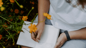 Person writing in a notebook surrounded by flowers, symbolizing reflection and the dopamine paradox.