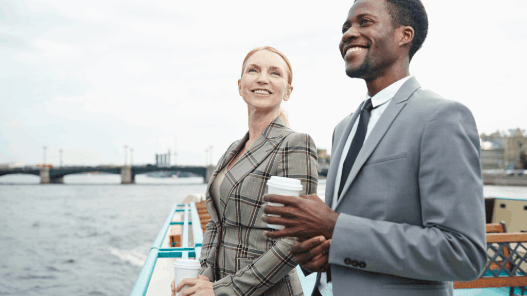 Two business professionals smiling and relaxing by the water, symbolizing balance and the choice to escape hustle culture.