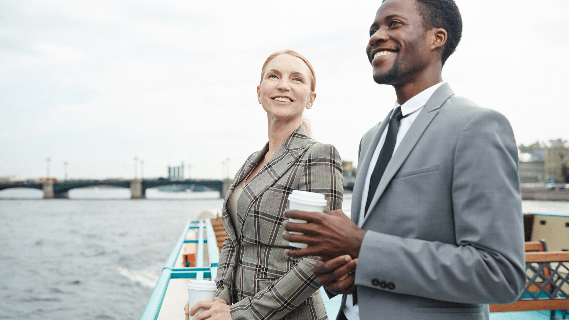 Two business professionals smiling and relaxing by the water, symbolizing balance and the choice to escape hustle culture.