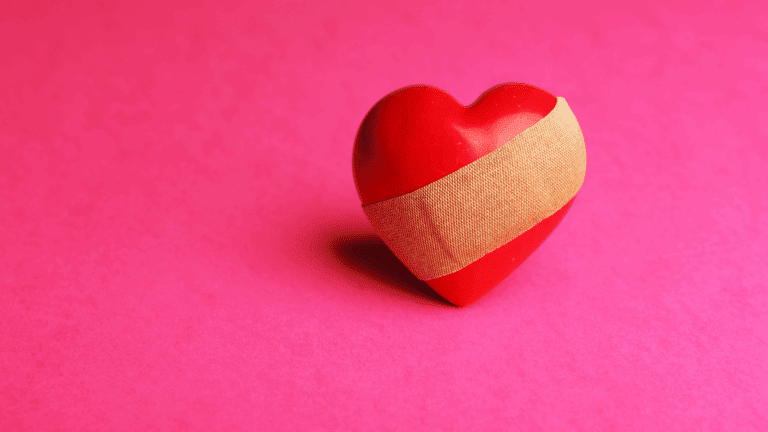 Red heart with a bandage symbolizing healing and the emotional process of recovering from a breakup.