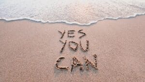 “Motivational words ‘Yes you can’ written in sand by the ocean, symbolizing optimism and the power of Dopamine Coaching Neuroscience.”