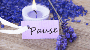 Lit lavender candle with purple flowers and a note reading “Pause,” symbolizing mindfulness and neuroplasticity through relaxation.