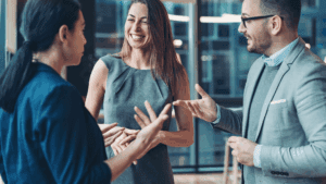 Three professionals smiling and talking in an office, demonstrating mindfulness and neuroplasticity through positive social connection.