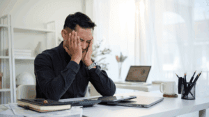 Stressed man sitting at desk with hands on face, showing workplace tension and the need for neuroscience-based anxiety relief.