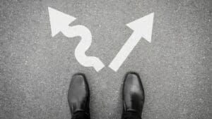 “Business shoes facing two arrows on pavement, symbolizing decision-making challenges addressed in Neuroscience-Based Executive Coaching.”