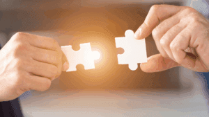 “Two hands connecting puzzle pieces with warm light, symbolizing human connection through Neuroscience-Based Executive Coaching.”